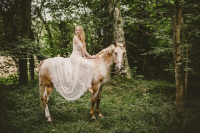 A bride sitting on a horse in a woodland.