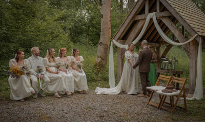 a couple getting married under an oak arbour in the woods at oakley, with 3 bridesmaids sitting nearby