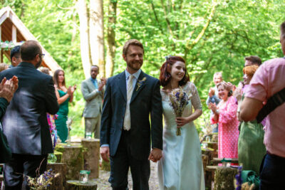 a bride and groom walk down the aisle together in a woodland wedding venue