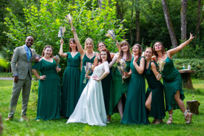 a bride poses with her bridesmaids in green dresses outside at a woodland wedding venue