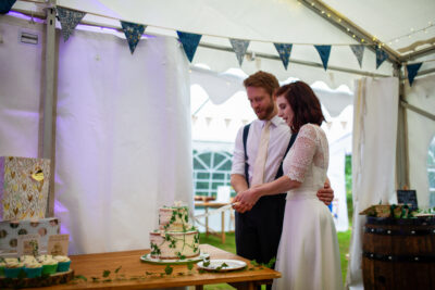 a bride and groom cut their wedding cake inside a marquee decorated with bunting