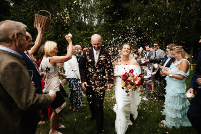 a bride and groom walk between their guests, who are throwing confetti