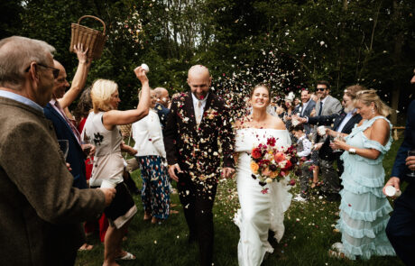 a bride and groom walk between their guests, who are throwing confetti