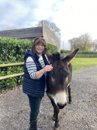 a woman smiling and stroking a donkey