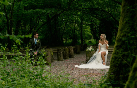 a bride and groom sit across from each other on benches in a woodland wedding venue