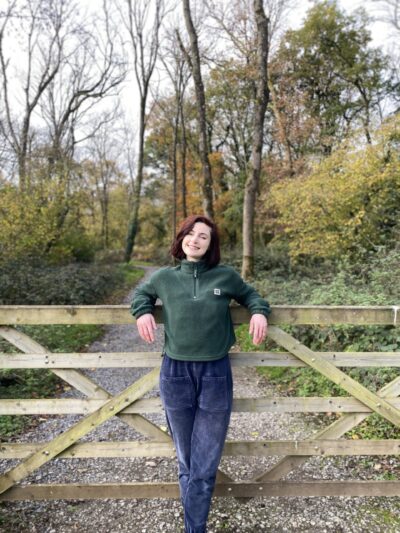 a girl smiling and leaning against a fence leading into a woodland