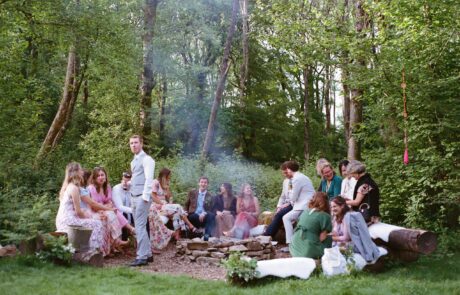 wedding guests sit around a firepit in a woodland