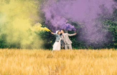 a bride and groom kiss in a field holding cannons with purple and yellow smoke coming out of them