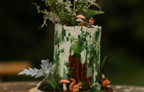 a forest themed wedding cake on a log slice with mushrooms, moss and trees iced on to it