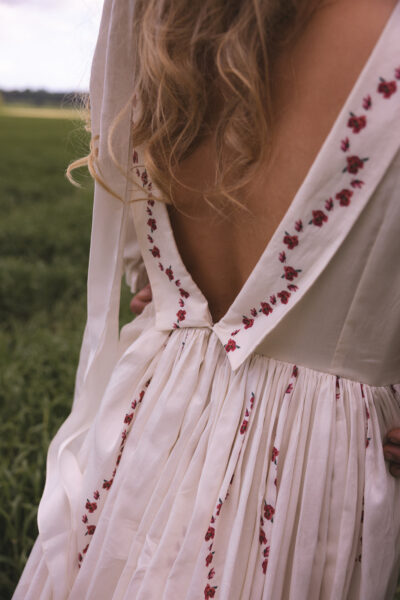 The back of a bride's wedding dress - she has long blonde hair and a white dress with red flowers embroidered on,