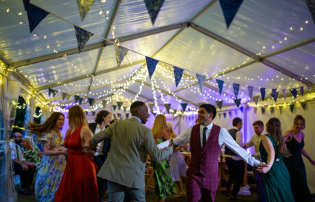 wedding guests dance under a marquee decorated with lights and bunting