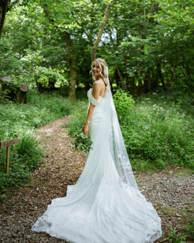 A bride stands in the woodlands at The Woods at Oakley in her wedding dress. She looks back at the camera.