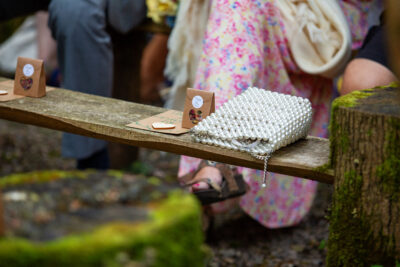 a confetti pack and handbag sit on a bench at a woodland wedding