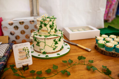 a white wedding cake with green ivy sits on a table with ivy, cupcakes and presents on it 