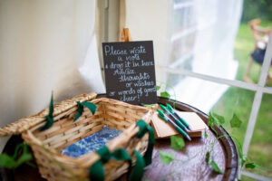 a basket, paper, pens and a sign asking guests to write a note sit on top of a barrel table