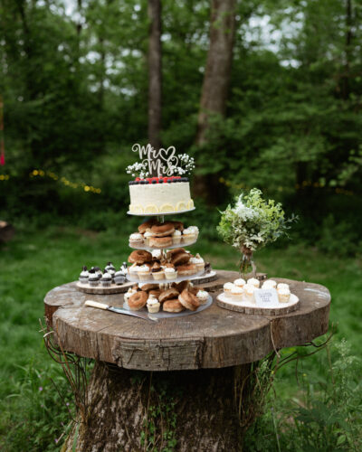 a wedding cake sits on a stump in a woodland