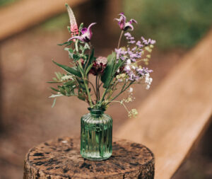 wildflowers in a glass posy jar on top of a wooden stump