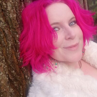 a photo of a woman with pink hair smiling and leaning against a tree