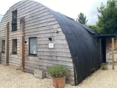 A converted world war 2 nissen hut with windows, plants and a gravel drive