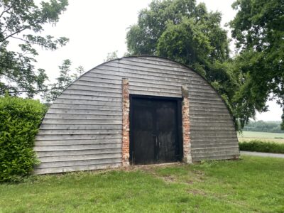 An old world war 2 nissen hut surrounded by trees and grass.