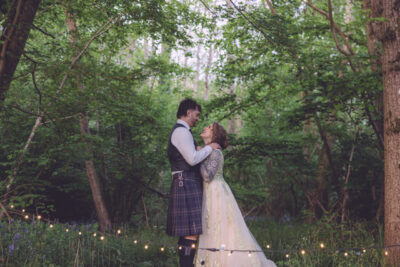 a bride and groom hold each other and look at each other in a woodland with fairy lights