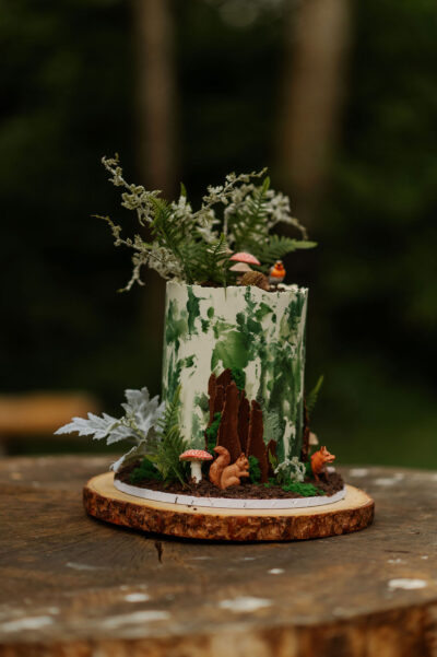 a woodland wedding cake decorated with sugared bark, mushrooms and animals on a wooden log slice