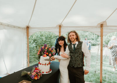 a bride and groom smile as they cut their wedding cake inside a marquee