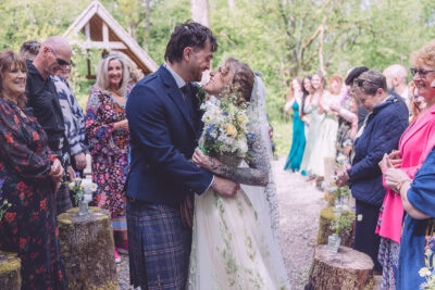 A bride and groom kiss as they walk down the aisle at a woodland wedding venue