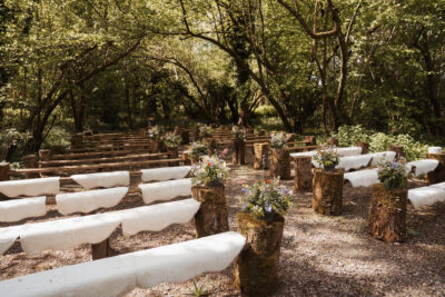 Benches with white rugs under a canopy of trees at a woodland wedding venue