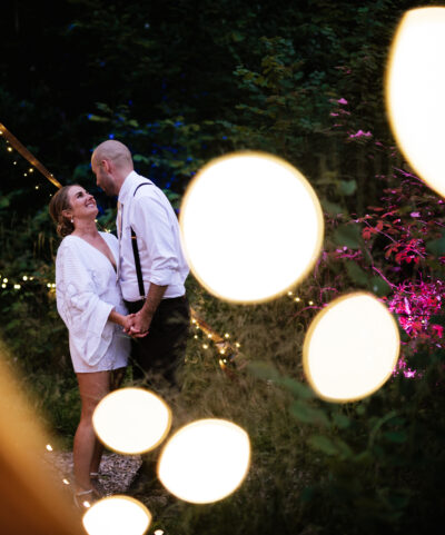 A bride and groom laugh together surrounded by fairy lights at dusk