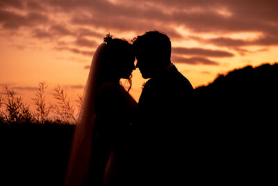 A silhouette of a bride and groom during sunset in a field