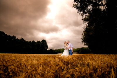 a bride and groom kiss in a field with dramatic grey clouds overhead
