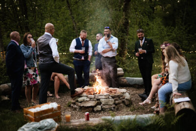 guests sit around a firepit at a woodland wedding