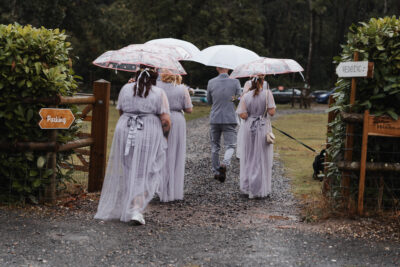 a bride and her bridesmaids walk along a path with white umbrellas